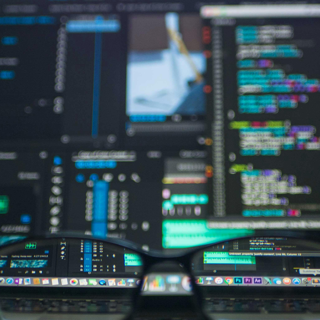 Close-up of computer screens displaying code and data, with glasses in the foreground reflecting parts of the screens. OCIDM,io Branding and Digital marketing Hamilton, Toronto, Oakville, Mississauga