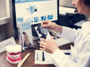 A dentist reviews a photograph at a desk with dental molds, brochures, and a computer screen displaying dental images, contemplating marketing strategies to grow your practice. OCIDM,io Branding and Digital marketing Hamilton, Toronto, Oakville, Mississauga