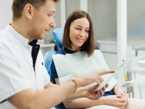 A dentist explains a procedure to a smiling patient in a dental office setting, demonstrating effective communication strategies that can help grow your practice. OCIDM,io Branding and Digital marketing Hamilton, Toronto, Oakville, Mississauga