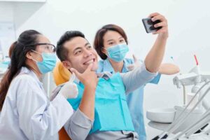 A man in a dental chair takes a selfie with two dentists, all wearing masks and gloves. This candid moment is perfect for boosting brand awareness through social media marketing. OCIDM,io Branding and Digital marketing Hamilton, Toronto, Oakville, Mississauga