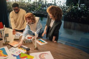 Three colleagues in a dental practice discuss charts and graphs on a table, including a small wind turbine model, as part of their rebranding strategy to attract more patients. OCIDM,io Branding and Digital marketing Hamilton, Toronto, Oakville, Mississauga