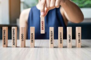 A person arranges wooden blocks labeled with marketing-related terms, with "BRAND" in focus, highlighting strategies for brand building on a table. OCIDM,io Branding and Digital marketing Hamilton, Toronto, Oakville, Mississauga