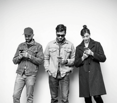 Three people standing against a wall, each looking at their smartphone. They appear to be engrossed in their screens. OCIDM,io Branding and Digital marketing Hamilton, Toronto, Oakville, Mississauga