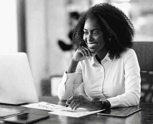 Person sitting at a desk, smiling at a laptop, with papers and a tablet nearby. OCIDM,io Branding and Digital marketing Hamilton, Toronto, Oakville, Mississauga