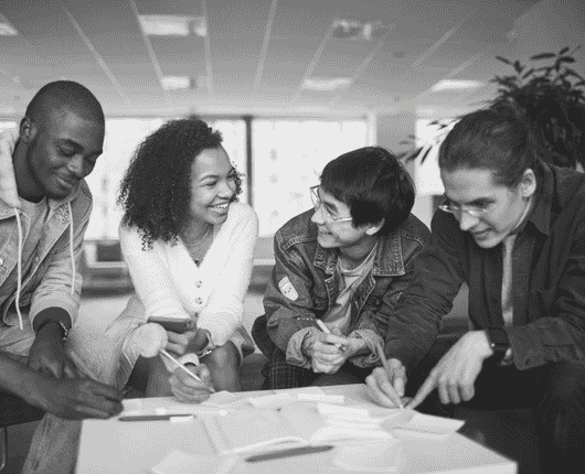 Four people are sitting and smiling, engaged in a collaborative discussion, with papers and pens on the table in front of them. OCIDM,io Branding and Digital marketing Hamilton, Toronto, Oakville, Mississauga